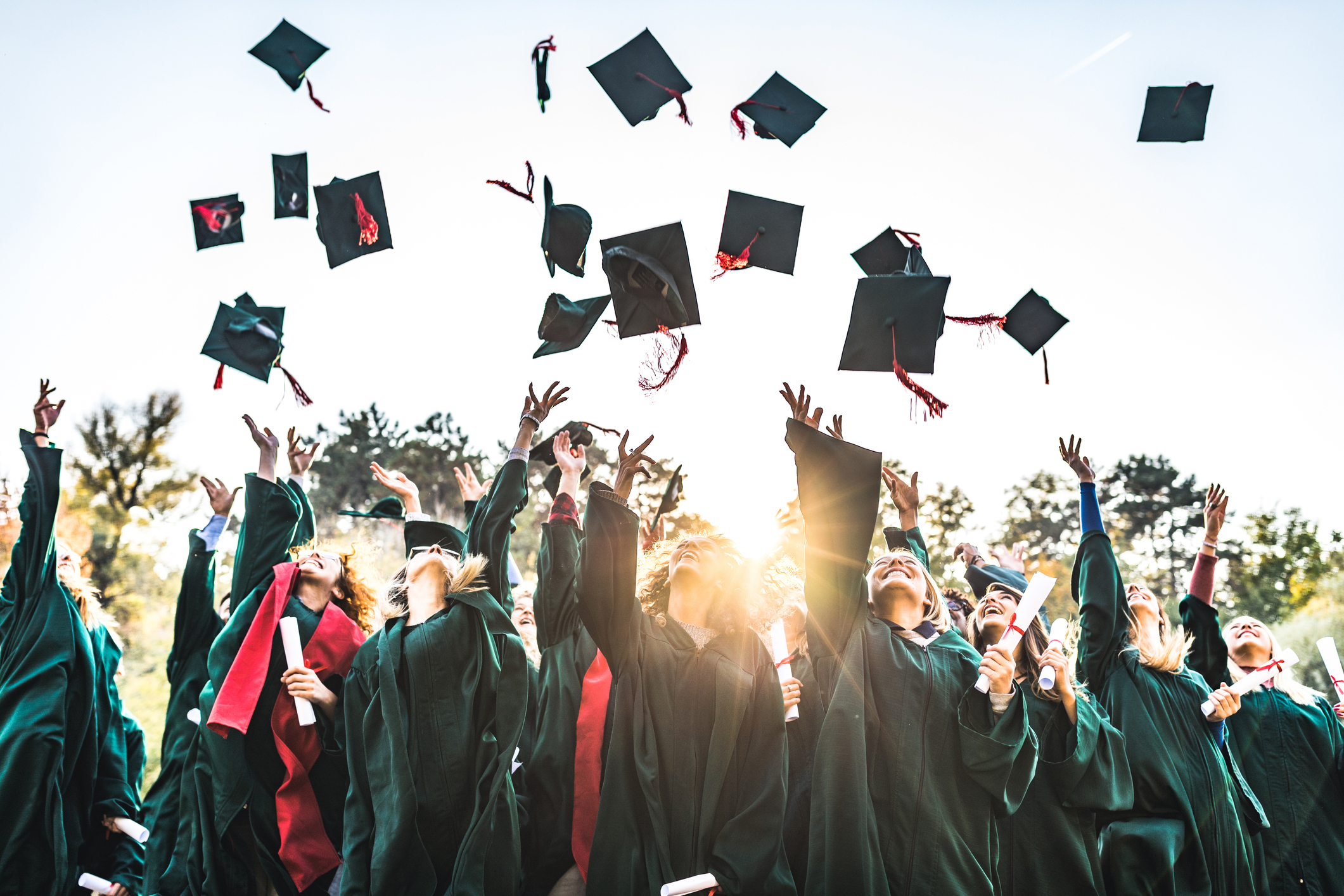 Students in graduation caps and gowns hold diplomas and smile as they throw their caps in the air.