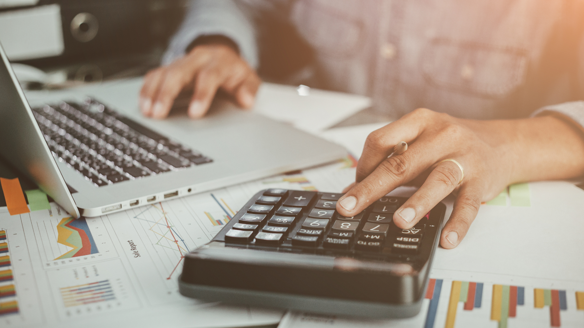 Person at a desk with budget documents using a laptop computer and a calculator. 