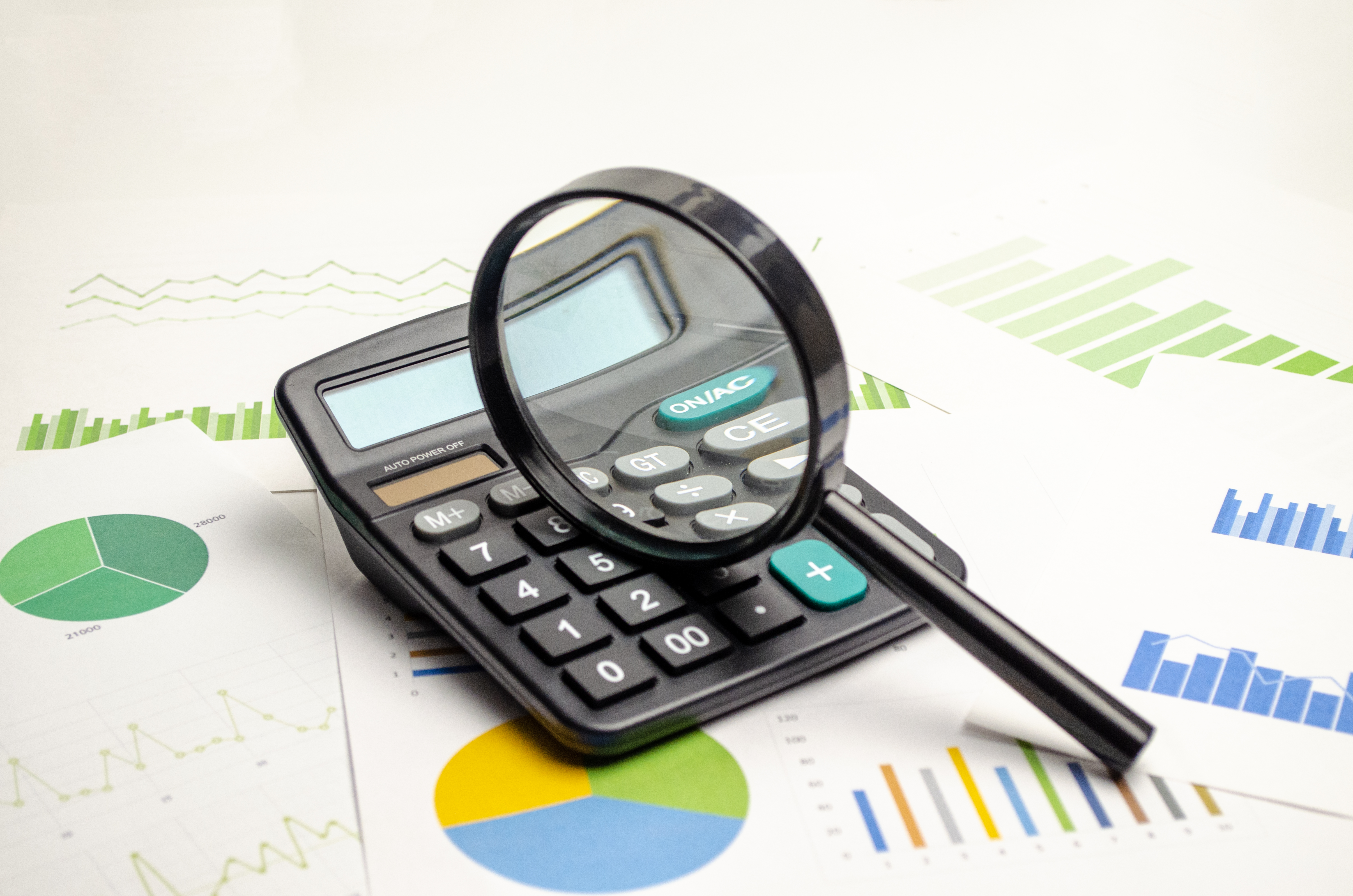 A magnifying glass on top of a calculator on top of many budget documents.