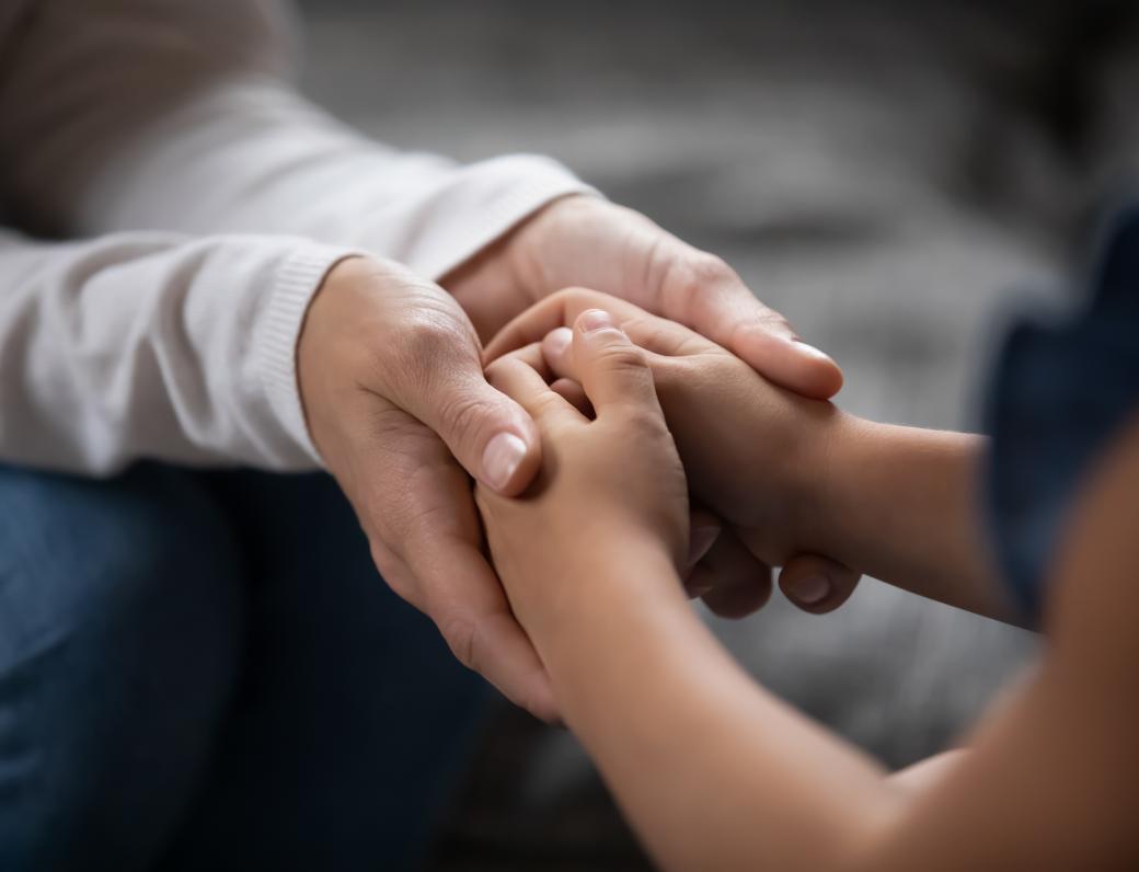 Two sets of hands; an adult holding a child's hands in both of their own.