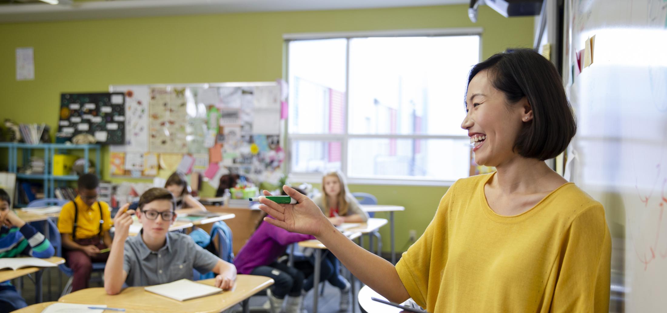 Happy female middle school teacher leading lesson in classroom.