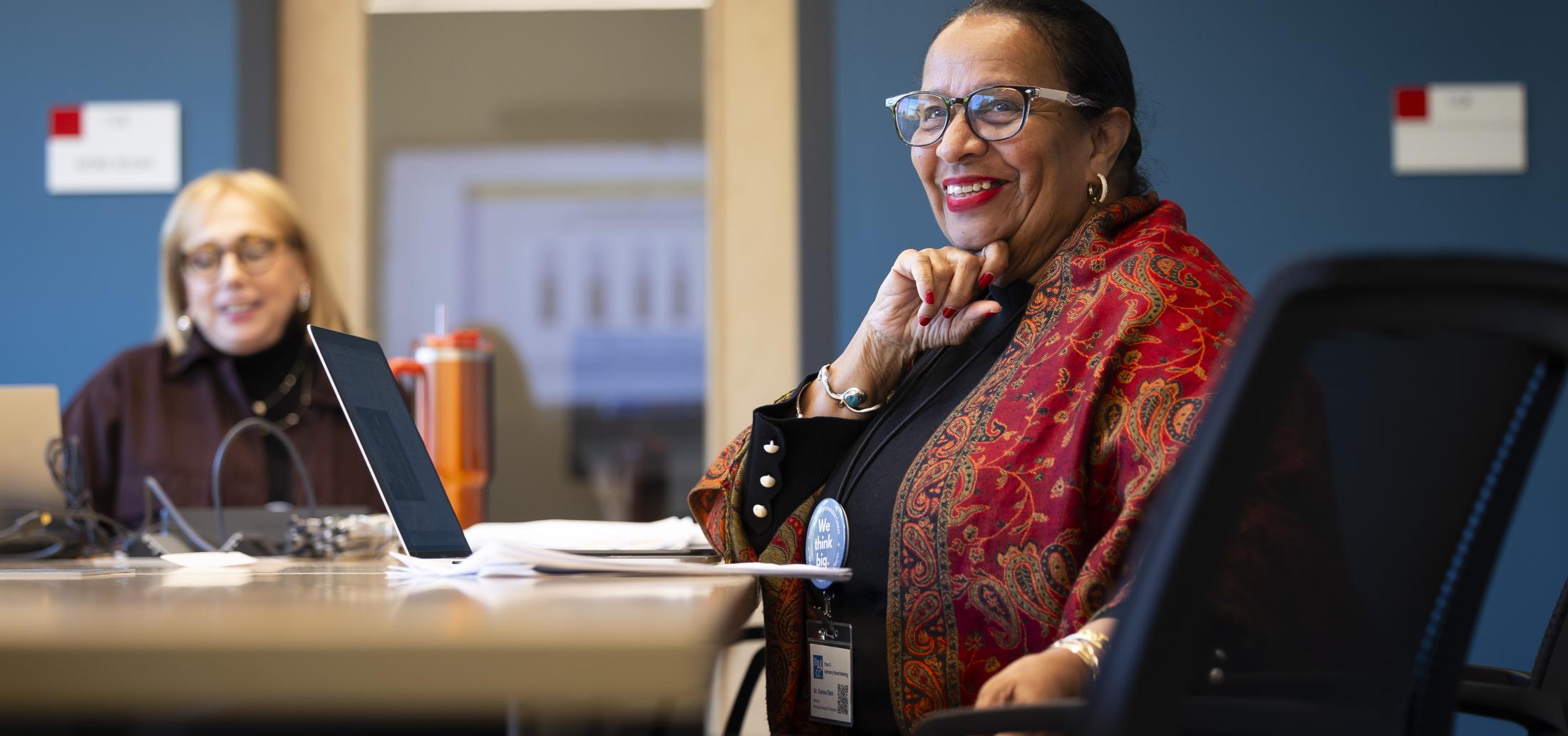 Dr. Donna Elam sitting at table smiling with her hand to her chin