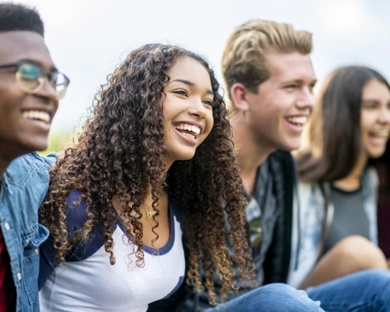 Four teenage students sit next to each other and smile.