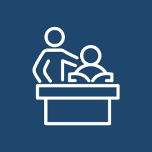 Icon of a teacher guiding a student at a desk, representing instruction and teaching support.